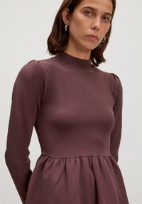 Langärmliges Kleid in dunklem Mauve, gerippte Textur, hoher Kragen, tailliertes Oberteil und schwingender Rock mit gerafftem Nahtdetail.