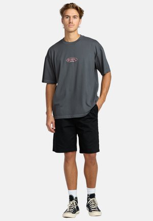 Short-sleeve gray t-shirt with red logo, paired with black shorts and black high-top sneakers. Simple design, relaxed fit.