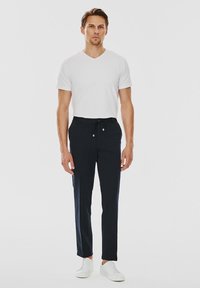 Biała koszulka z dekoltem w serek w połączeniu z ciemnoniebieskimi, zwężającymi się spodniami z elastycznym pasem i bocznymi kieszeniami. Model nosi białe trampki.