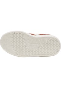 Sneakersula med en strukturerad vit gummiyta, som har cirkulära prickar och zickzackmönster för grepp; bruna accenter synliga.