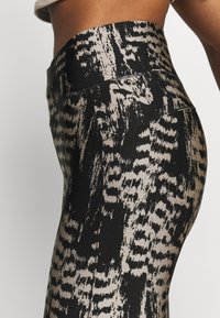 Svarta och beige mönstrade leggings har en hög midja, en slät tygstruktur och en tajt passform.