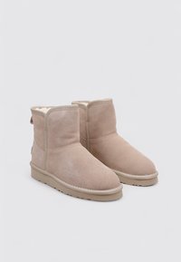 Botines beige de ante con forro de piel suave, punta redonda y suela plana de goma, con una costura decorativa y diseño minimalista.