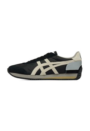 Baskets basses noires et beige avec des bandes blanches sur le côté, un patch gris au talon et une semelle noire nervurée, vues de profil gauche.