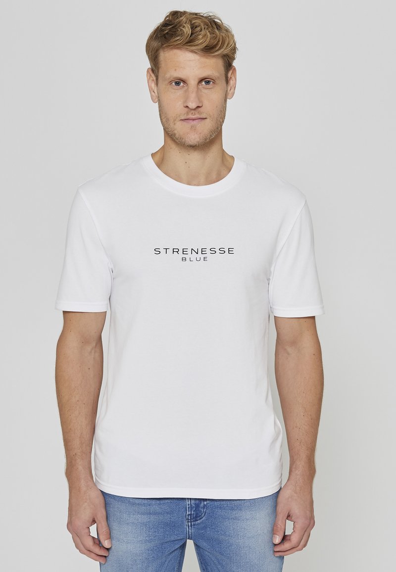 T-shirt blanc à manches courtes avec le texte "STRENESSE BLUE" en noir sur la poitrine. En coton, avec un col rond et une coupe décontractée.