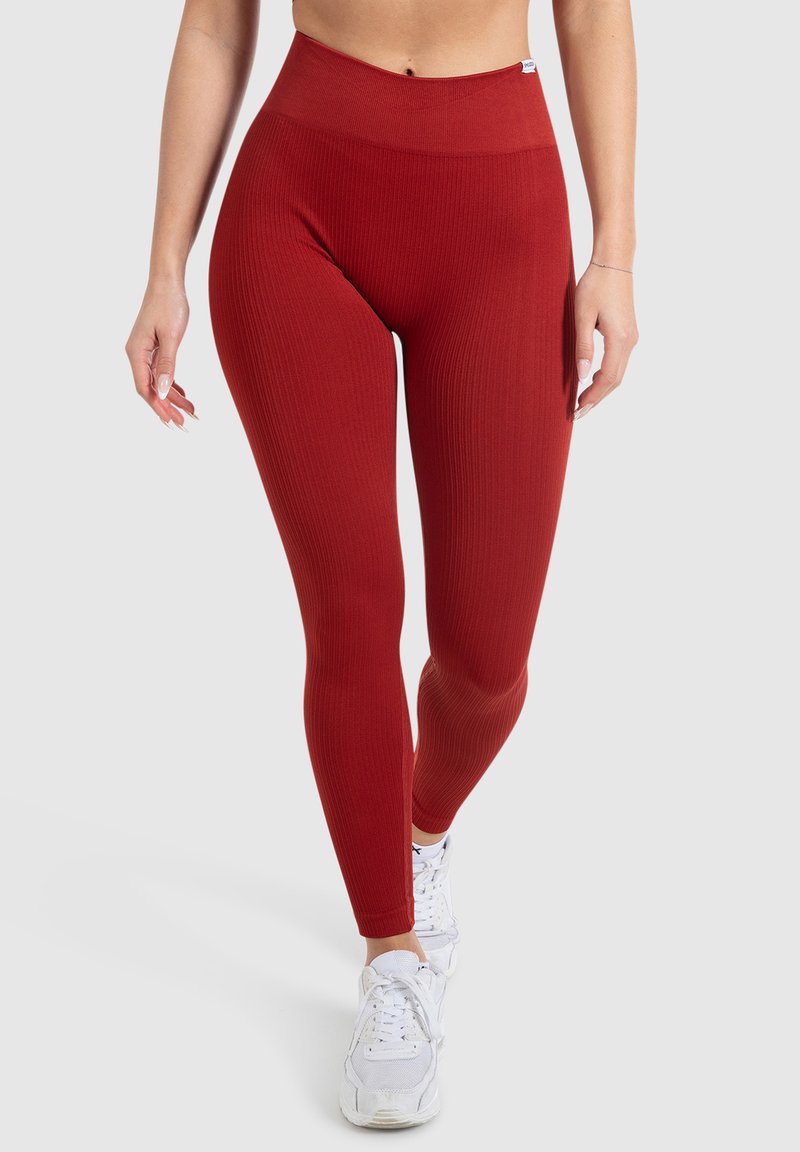 Rote gerippte Leggings mit einem hohen Bund, die eine glatte Textur und einen figurbetonten Schnitt aufweisen, kombiniert mit weißen Sportschuhen.