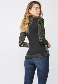 Langärmliger Pullover in Schwarz mit strukturierten, grün floral gemusterten Ärmeln. Rippensaum, taillierte Passform und ein glatter Körperbereich.