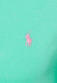Mentolově zelená bavlněná košile s malým růžovým vyšitým logem polo hráče na hrudi, s ribovanou texturou.