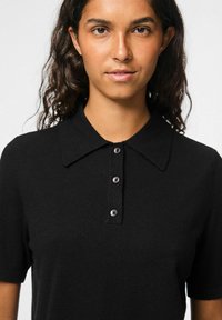 Black polo shirt with a soft texture, featuring a collared neck and short sleeves. Five button detail on the front is visible.