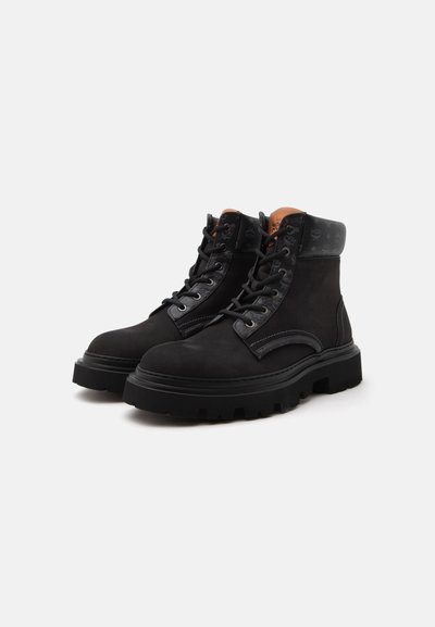 Bottes en cuir noir à lacets avec semelles épaisses et col matelassé, présentées côte à côte sur un fond blanc.