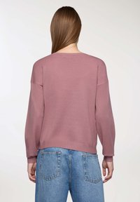 Pullover in rosa polveroso, realizzato in morbido tessuto testurizzato con una vestibilità ampia, caratterizzato da spalle scese e polsini a costine, abbinato a jeans blu.
