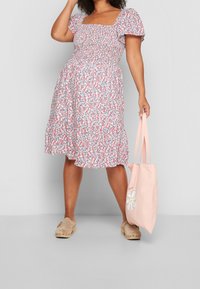 Blumen-Midikleid mit kurzen Puffärmeln, quadratischem Ausschnitt und gerafftem Oberteil. Kombiniert mit einer rosa Tasche im Gänseblümchen-Design.