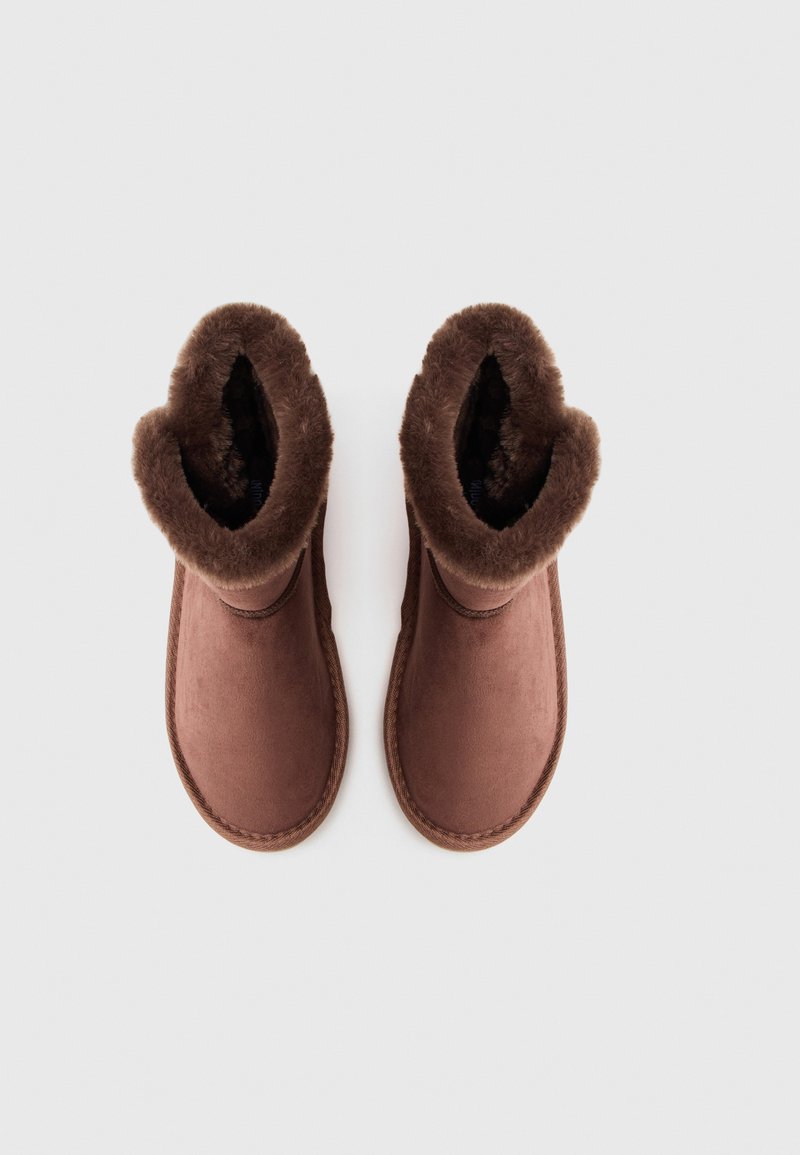 Bruine laarzen met een zachte, faux fur voering en buitenkant. Ronde neus met een lage enkelhoogte en contrasterende stiksels langs de zool.