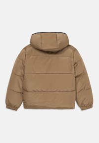 Doudoune marron avec capuche, présentant un design matelassé et des poignets élastiques. Le matériau a une texture et un éclat subtils.