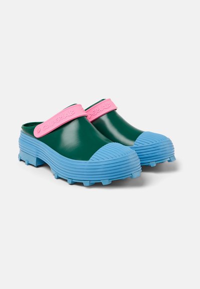 Zoccoli in gomma verde con superficie testurizzata, suola rigata blu e una cinghia rosa con il nome del marchio. Design chunky adatto per l'uso all'aperto.