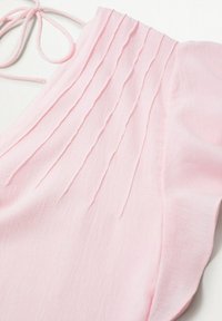 Tessuto rosa chiaro con pieghe verticali e dettaglio di un nastro annodato, che suggerisce un indumento o accessorio dalla morbida texture.