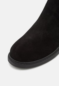 Svart mocka ankle boot med rund tå och en hållbar svart gummisula med synlig sömnadsdetalj. Slät textur överlag.