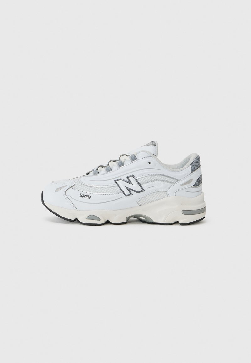 Chaussure de sport blanche avec des superpositions en mesh et en matériau synthétique, de forme courbée, avec des accents gris, une semelle épaisse et un logo "N" bien visible sur le côté.