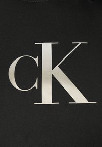 Felpa nera con un grande logo "CK" riflettente in argento stampato con un font moderno sul davanti. Texture morbida, design casual.