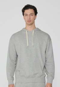 Grauer Kapuzenpullover aus weichem Material, mit einer Fronttasche, gerippten Bündchen und Kordeln in contrasting heller Farbe.