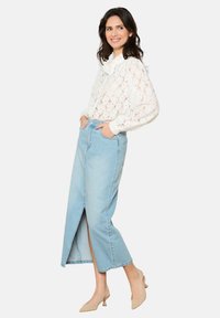 Bela čipkasta bluzica z nabranim izrezom, v kombinaciji s svetlo modrim jeans krilom z razporkom spredaj. Model nosi bež čevlje na blok peto.