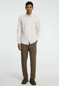 Camisa de rayas de manga larga en colores claros, combinada con pantalones en verde oliva. La camisa tiene un cuello abotonado y un corte ajustado.