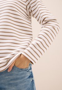 Camiseta de manga larga a rayas en blanco y marrón claro. Tejido suave con rayas horizontales, cuenta con un corte relajado y un escote redondo.