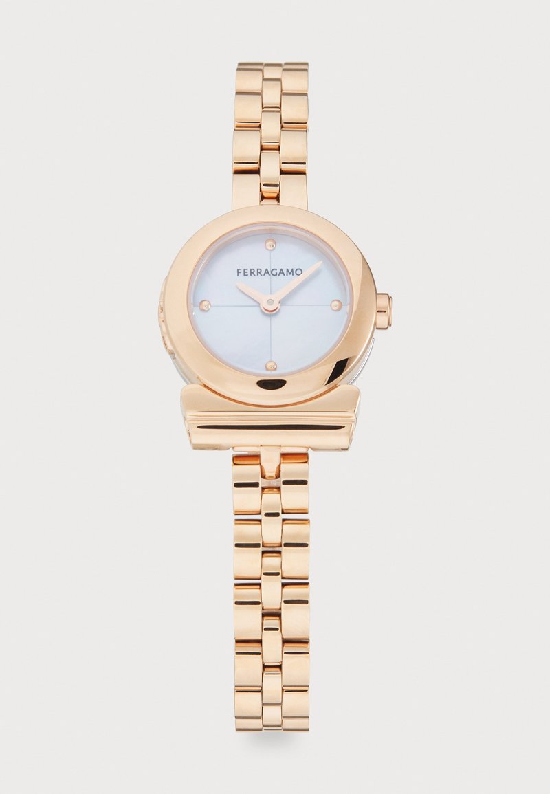 Kuldne metallkell ümmarguse näo, helesinise diali ja minimalistliku disainiga. Omab lingitud randme rihma ja brändi logo, mis on paigutatud näo peale.