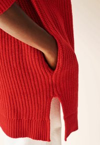 Maglione rosso lavorato a maglia con texture a coste, tasca laterale e spacchi laterali all'orlo; presenta una vestibilità comoda.