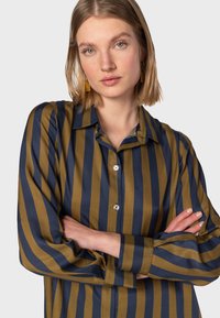 Camicia button-up con strisce verticali blu navy e verde oliva, maniche lunghe e colletto classico con una leggera lucentezza.