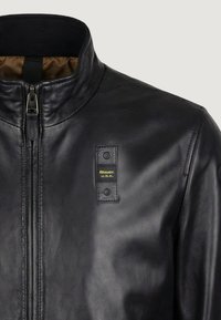 Zwarte leren jas met hoge kraag, ritssluiting aan de voorkant en een klein gestikt patch met het label "Blauer U.S.A." op de borst.