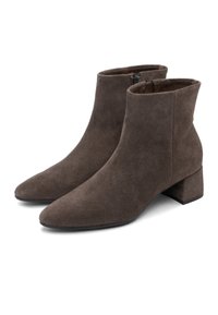Ett par bruna mocka ankelstövlar med klackar och sidogrepp, uppställda på en vit bakgrund.
