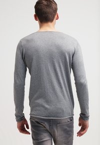 T-shirt grigio a maniche lunghe con scollo rotondo, design aderente e tessuto morbido. Indossato con jeans grigi, mostrato da dietro.