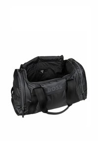 Black duffel bag with a smooth, matte finish, featuring dual straps, a zipper closure, and a prominent embossed logo on the side.