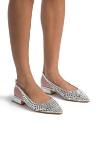 Bailarinas plateadas con tiras traseras y punta afilada, que presentan una malla de pequeños rhinestones. Tacón bajo y parte trasera suave.