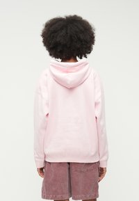 Haut à capuche rose avec cordon de serrage et coupe ample, associé à un short en velours côtelé rose clair. Texture douce, style décontracté et manches courtes.