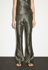 Olivgrön tvådelad outfit i skimrande tyg; har en omlottopp med sidoknytning och utsvängda byxor med en slät textur.