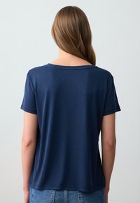 Granatowa koszulka z krótkim rękawem o luźnym kroju i okrągłym dekoltem, wykonana z miękkiego, gładkiego materiału. Widok z tyłu przedstawia prosty wzór.