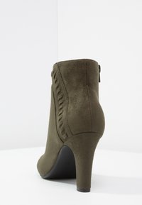 Kotníková bota z olivově zeleného semiše se špičatou špičkou, vysokým jehlovým podpatkem a dekorativním bočním prošitím. Uzavírá se zipem na zadní straně.
