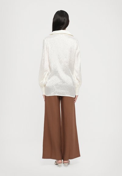 Cream textured blouse with a collar, long puff sleeves; paired with high-waisted brown wide-leg trousers and neutral shoes.