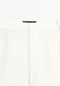White garment waistband with central seam and a partially visible black label at the top center.