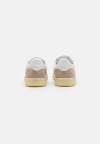 White leather sneakers with beige suede accents, rounded edges, and a smooth rubber sole. Back view shows scalloped design on the heel.
