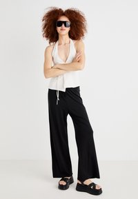 White halter top, black wide-leg pants, and chunky black sandals. Model wears oversized black sunglasses, showcasing a casual outfit.