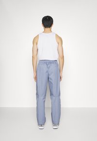 Pantaloni azzurri chiari, morbidamente aderenti, con una cintura elastica, abbinati a un top senza maniche bianco, visti da dietro, indossati con sneakers bianche.