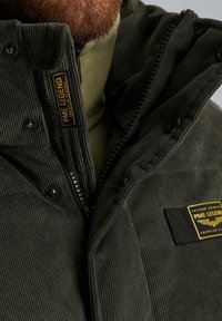 Donkergroene corduroy jas met een frontzipper, zwarte knopen en een PME Legend label. Beschikt over een gestructureerd oppervlak en een gedeeltelijke capuchon.