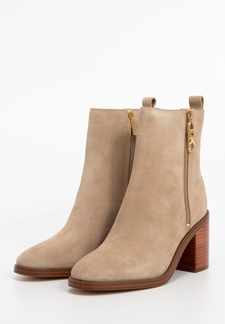 Bottes en daim beige à la cheville avec un bout pointu, des zips sur les côtés, des accents en métal doré et un talon bloc marron. Texture lisse et design minimaliste.