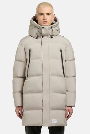 Lichtbeige pufferjack met een grote capuchon, ritszakken aan de zijkanten en gestepte panelen. Bevat trekkoorden en een logo patch aan de onderkant.