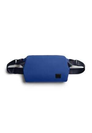 Sac banane rectangulaire bleu avec une sangle noire réglable et un petit écusson logo noir à l'avant, présenté sur fond blanc.