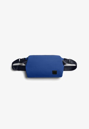 Sac banane rectangulaire bleu avec une sangle noire réglable et un petit écusson logo noir à l'avant, présenté sur fond blanc.