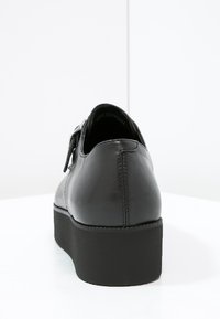 Chaussure en cuir noir à petit talon, de forme arrondie et à finition lisse. Dotée d'une boucle décorative et d'une semelle en caoutchouc robuste.