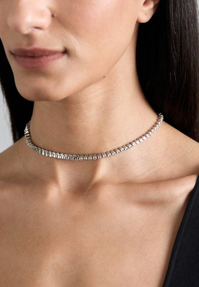 Srebrna choker z naszyjnikiem z rzędem błyszczących kryształów, osadzonych na gładkim metalowym łańcuszku o gładkim, polerowanym wykończeniu.
